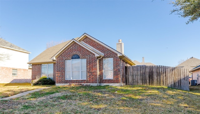 view of front facade with fence, central AC unit, a front lawn, and brick siding