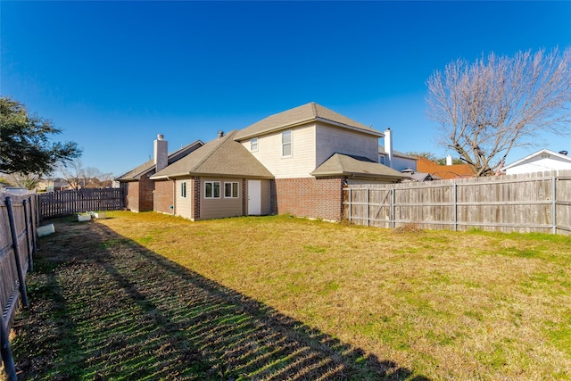 back of house featuring a yard, a fenced backyard, a chimney, and brick siding