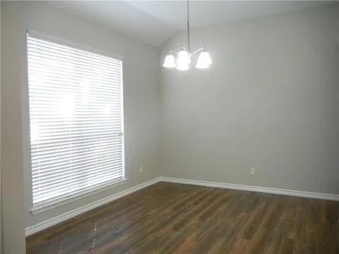 spare room with dark hardwood / wood-style floors and an inviting chandelier