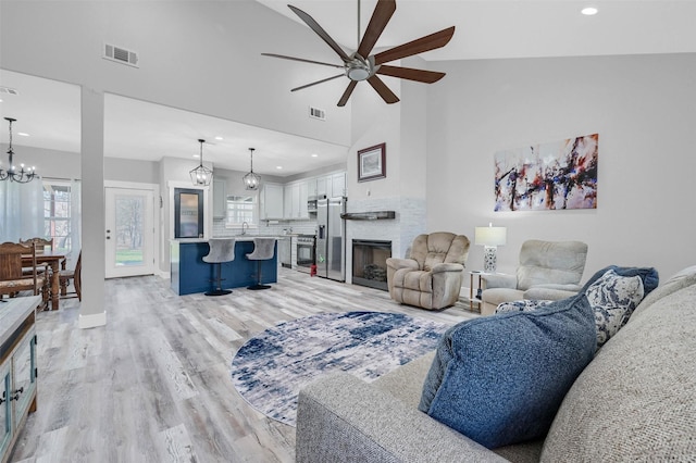 living room with ceiling fan with notable chandelier, high vaulted ceiling, light hardwood / wood-style floors, and sink