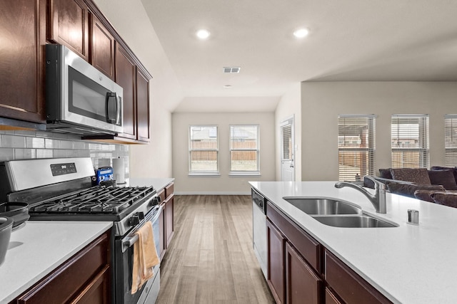 kitchen featuring appliances with stainless steel finishes, sink, backsplash, dark brown cabinetry, and light hardwood / wood-style floors