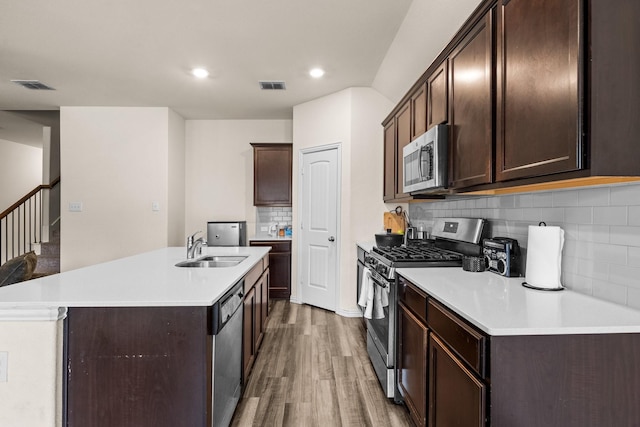 kitchen with sink, appliances with stainless steel finishes, hardwood / wood-style floors, dark brown cabinets, and a center island with sink