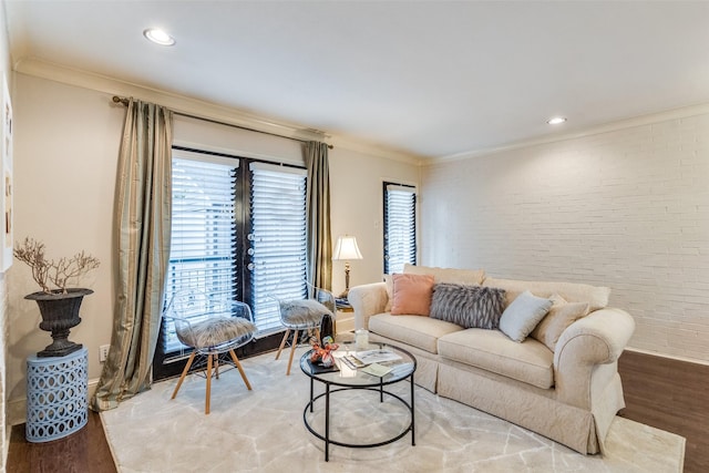 living room featuring hardwood / wood-style flooring, crown molding, and brick wall