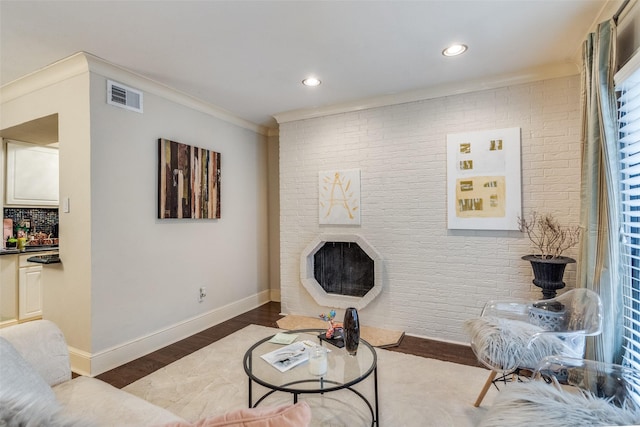 living room with hardwood / wood-style flooring, a fireplace, ornamental molding, and brick wall