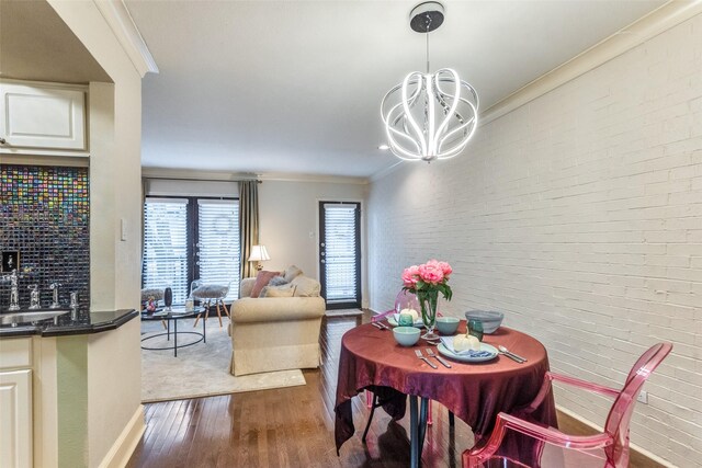 dining space with sink, crown molding, dark hardwood / wood-style floors, brick wall, and a chandelier