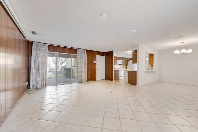 unfurnished living room with a textured ceiling, a notable chandelier, wooden walls, and light tile patterned floors