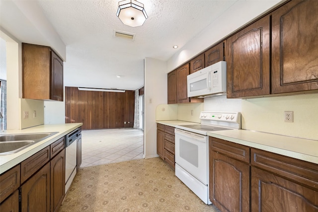 kitchen featuring sink, dark brown cabinets, a textured ceiling, wooden walls, and white appliances