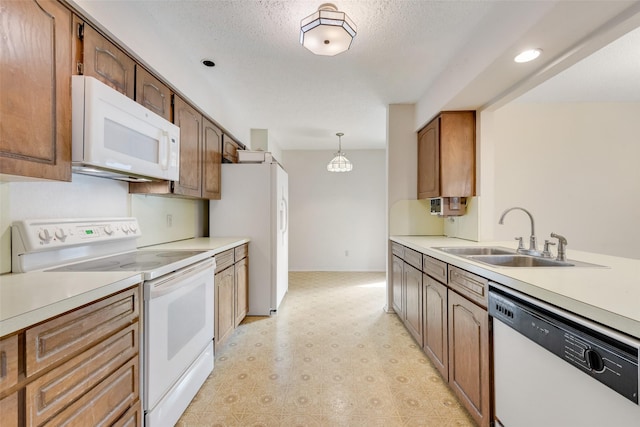 kitchen featuring sink, white appliances, hanging light fixtures, and a textured ceiling