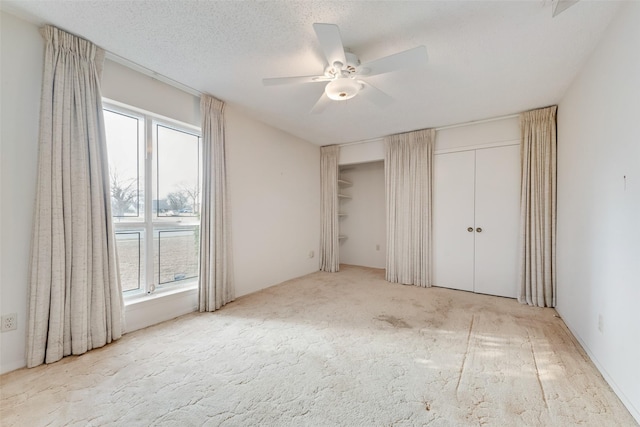 unfurnished bedroom featuring ceiling fan, two closets, light colored carpet, and a textured ceiling