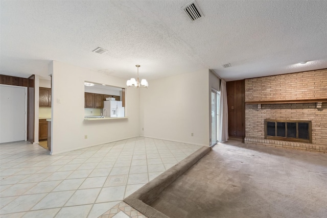 unfurnished living room featuring a chandelier, a textured ceiling, a brick fireplace, and light tile patterned floors