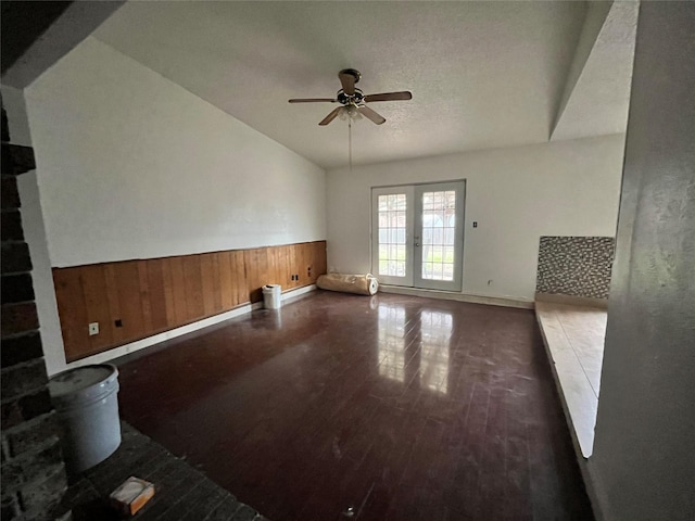 interior space with wooden walls, wainscoting, dark wood-type flooring, vaulted ceiling, and french doors