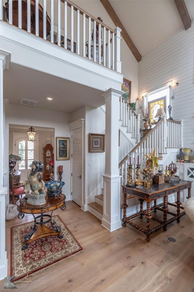 foyer entrance with ornate columns, beam ceiling, high vaulted ceiling, and light wood-type flooring