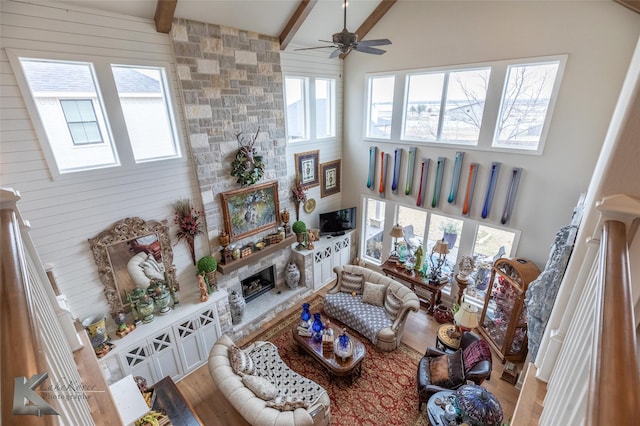 living room featuring a stone fireplace, high vaulted ceiling, hardwood / wood-style flooring, ceiling fan, and beam ceiling