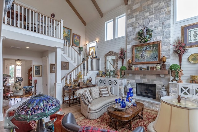 living room with beamed ceiling, a stone fireplace, high vaulted ceiling, and light wood-type flooring