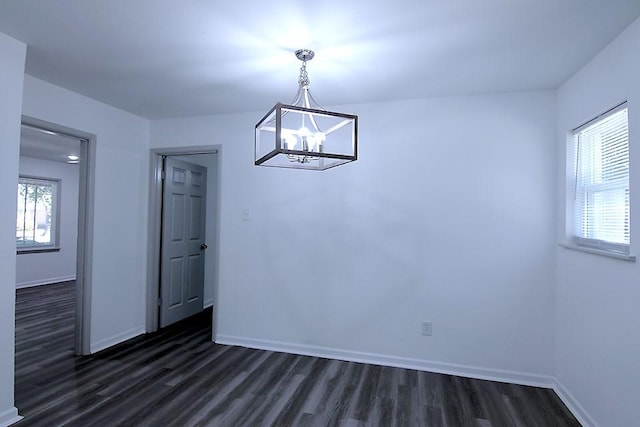 unfurnished dining area featuring plenty of natural light, dark wood-type flooring, and a chandelier