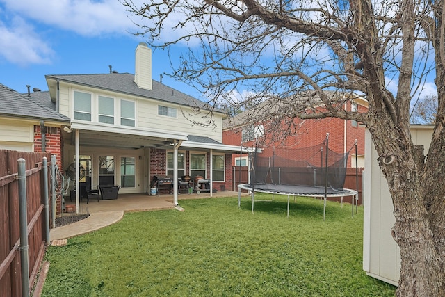 back of property with a trampoline, a yard, and a patio