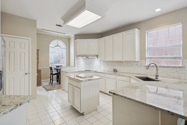 kitchen with tasteful backsplash, sink, hanging light fixtures, a center island, and light stone countertops