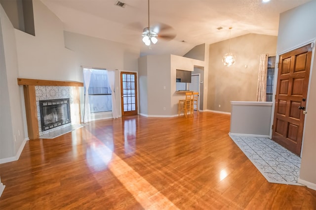 unfurnished living room with high vaulted ceiling, wood-type flooring, a tile fireplace, and ceiling fan