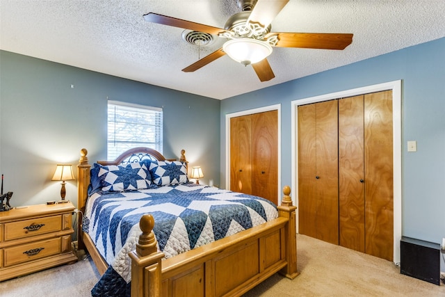 carpeted bedroom featuring ceiling fan, two closets, and a textured ceiling