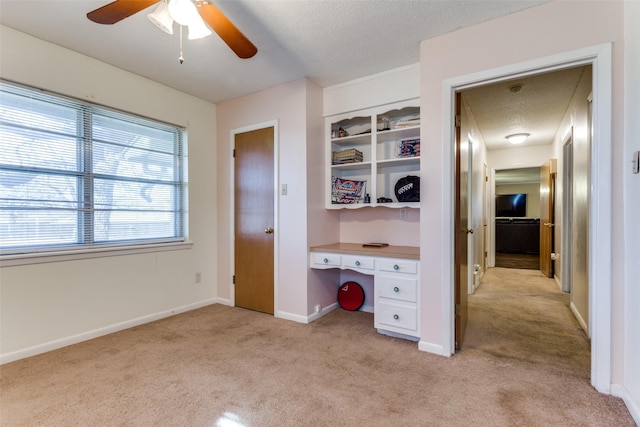 unfurnished office featuring ceiling fan, light colored carpet, built in desk, and a textured ceiling