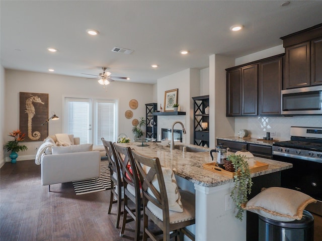 kitchen featuring stainless steel appliances, dark wood-type flooring, open floor plan, dark brown cabinetry, and a kitchen bar