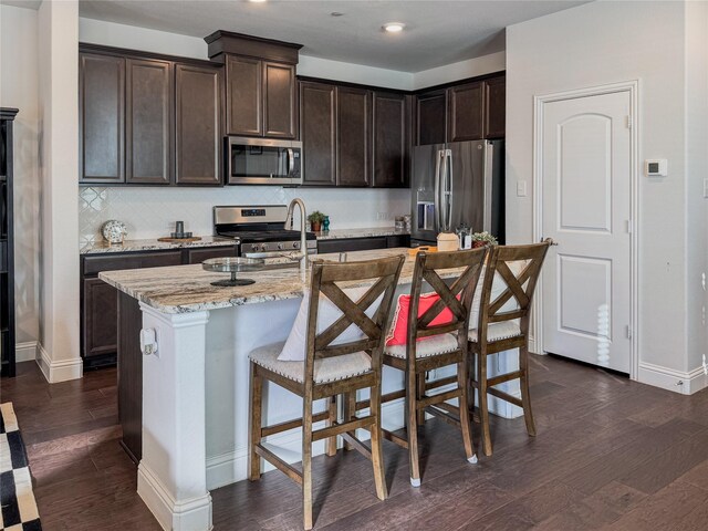 kitchen with dark wood-type flooring, light stone countertops, stainless steel appliances, dark brown cabinets, and a sink