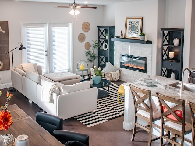 living room featuring a ceiling fan, a glass covered fireplace, baseboards, and wood finished floors