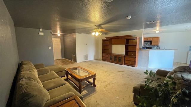 living room featuring ceiling fan, light colored carpet, and a textured ceiling