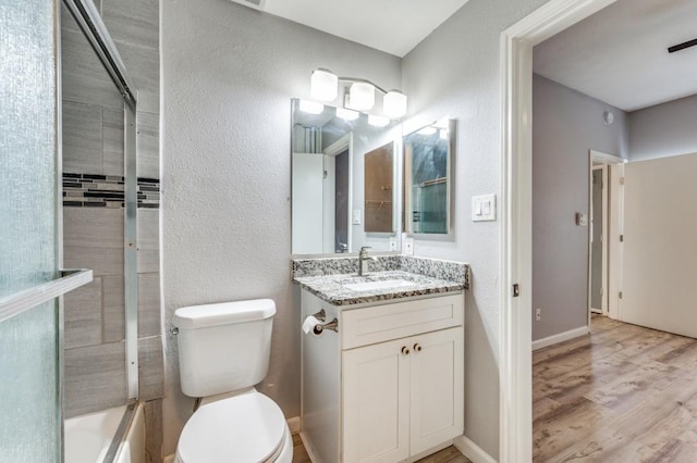 full bathroom featuring hardwood / wood-style flooring, vanity, shower / bath combination with glass door, and toilet