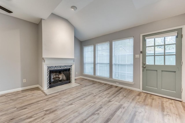 unfurnished living room featuring a fireplace, vaulted ceiling, and light hardwood / wood-style floors