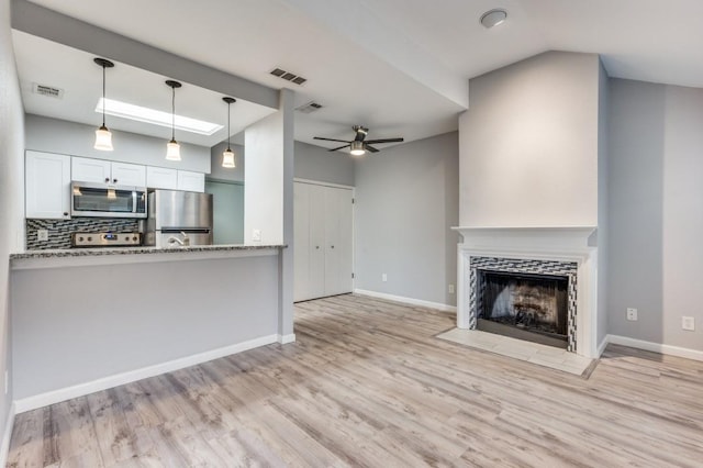 unfurnished living room featuring a fireplace, vaulted ceiling, ceiling fan, and light wood-type flooring