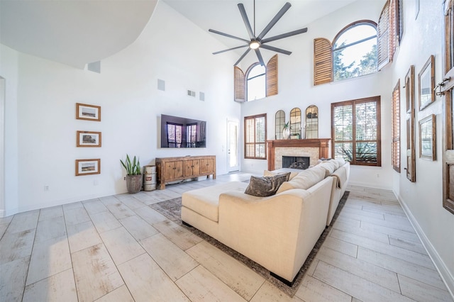 720 Amistad Dr, Prosper, TX 75078 - living room featuring a ceiling fan, a fireplace, light wood-style flooring, a towering ceiling, and baseboards