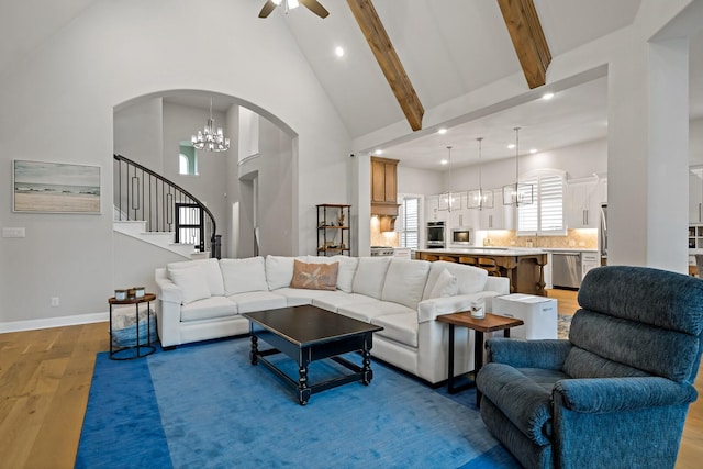 living room with beam ceiling, ceiling fan with notable chandelier, hardwood / wood-style floors, and high vaulted ceiling