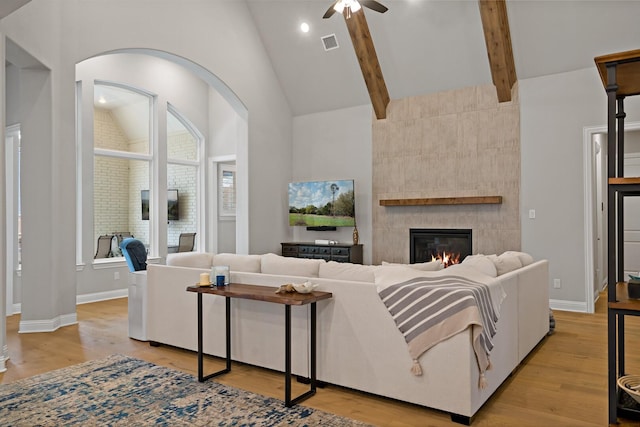 living room featuring light hardwood / wood-style flooring, ceiling fan, high vaulted ceiling, a fireplace, and beamed ceiling