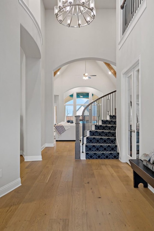 entrance foyer with ceiling fan with notable chandelier, wood-type flooring, and a high ceiling