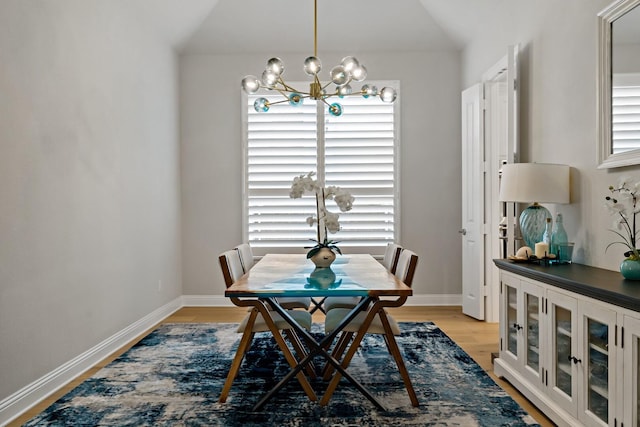 dining area with lofted ceiling, light wood-type flooring, and an inviting chandelier