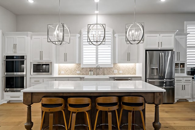 kitchen featuring sink, stainless steel appliances, white cabinets, a kitchen island, and light wood-type flooring