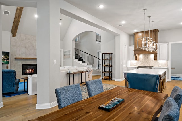 dining room featuring beam ceiling, a chandelier, a fireplace, and light hardwood / wood-style flooring