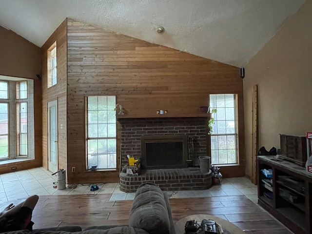 living room featuring wooden walls, high vaulted ceiling, a brick fireplace, and a textured ceiling