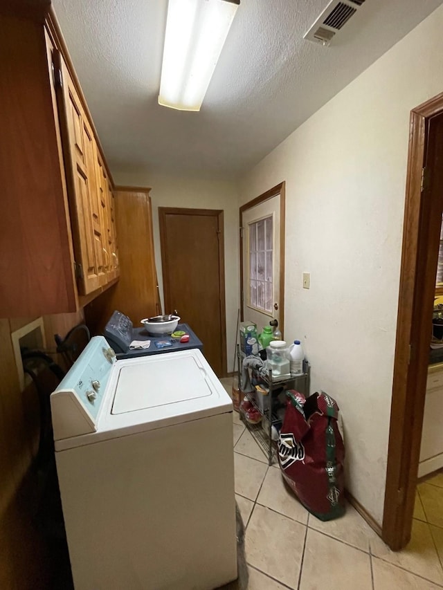 clothes washing area featuring light tile patterned floors, washer and clothes dryer, cabinets, and a textured ceiling