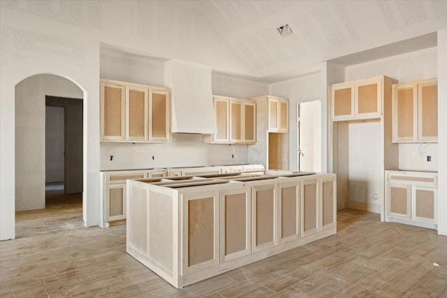 kitchen featuring arched walkways, light brown cabinets, visible vents, light wood-type flooring, and an island with sink