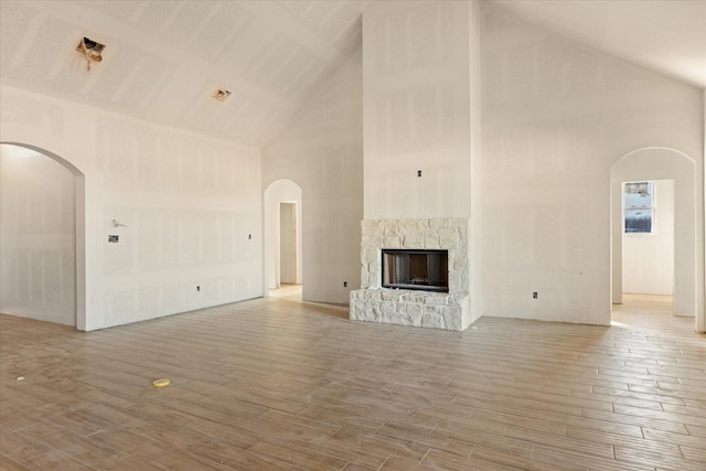 unfurnished living room featuring high vaulted ceiling, arched walkways, wood finished floors, and a stone fireplace