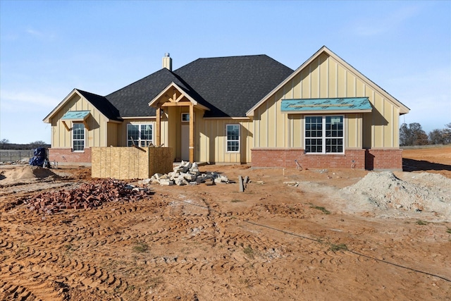 view of front of house with a shingled roof, a chimney, board and batten siding, and brick siding