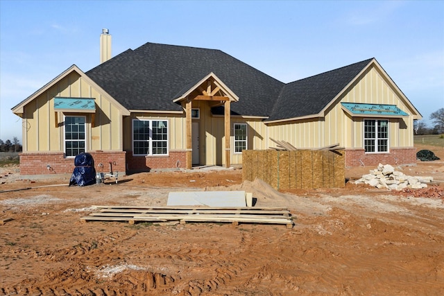 view of front of house featuring roof with shingles, brick siding, board and batten siding, and a chimney