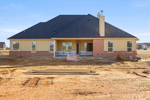 back of property with a shingled roof, brick siding, and a chimney