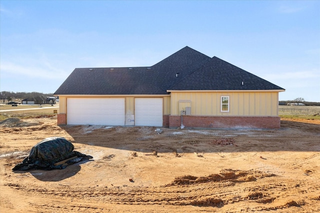 rear view of property featuring driveway, brick siding, and roof with shingles