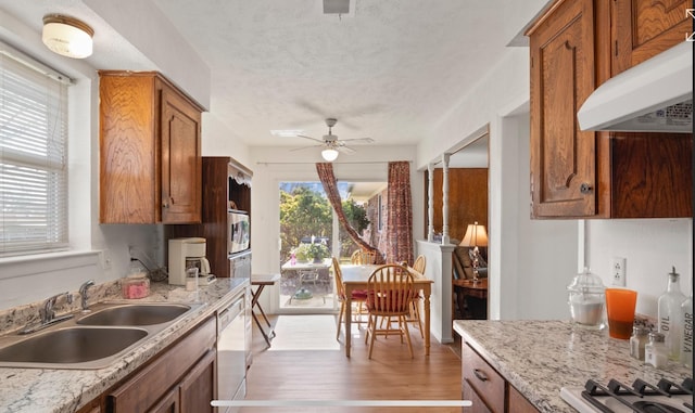 kitchen featuring range hood, sink, light stone counters, white dishwasher, and light hardwood / wood-style flooring