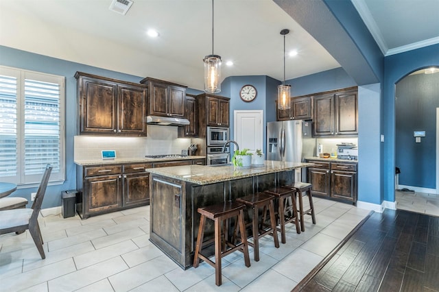 kitchen featuring appliances with stainless steel finishes, a breakfast bar, a kitchen island with sink, and dark brown cabinets