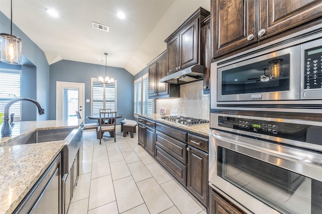 kitchen featuring lofted ceiling, appliances with stainless steel finishes, dark brown cabinetry, light stone countertops, and decorative light fixtures