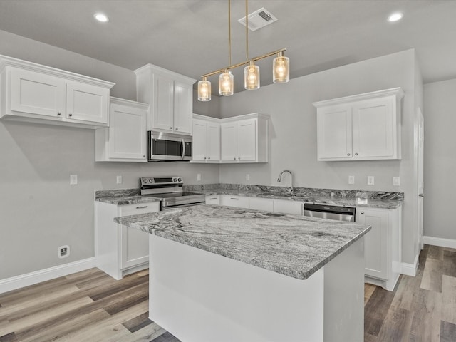 kitchen with appliances with stainless steel finishes, sink, white cabinets, and decorative light fixtures